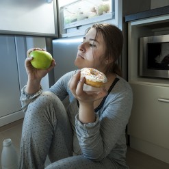 woman choosing between apple and donut at evening lunch